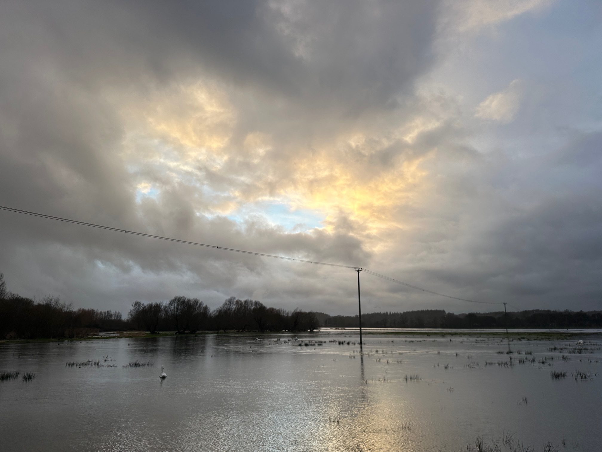 Photographic image of telegraph pole and wires standing proud of the floodwater against a changing sky