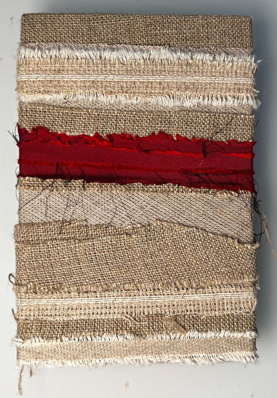 photograph of multiple fabrics over wood, mostly beige and off white, with a line of red silk in the middle.