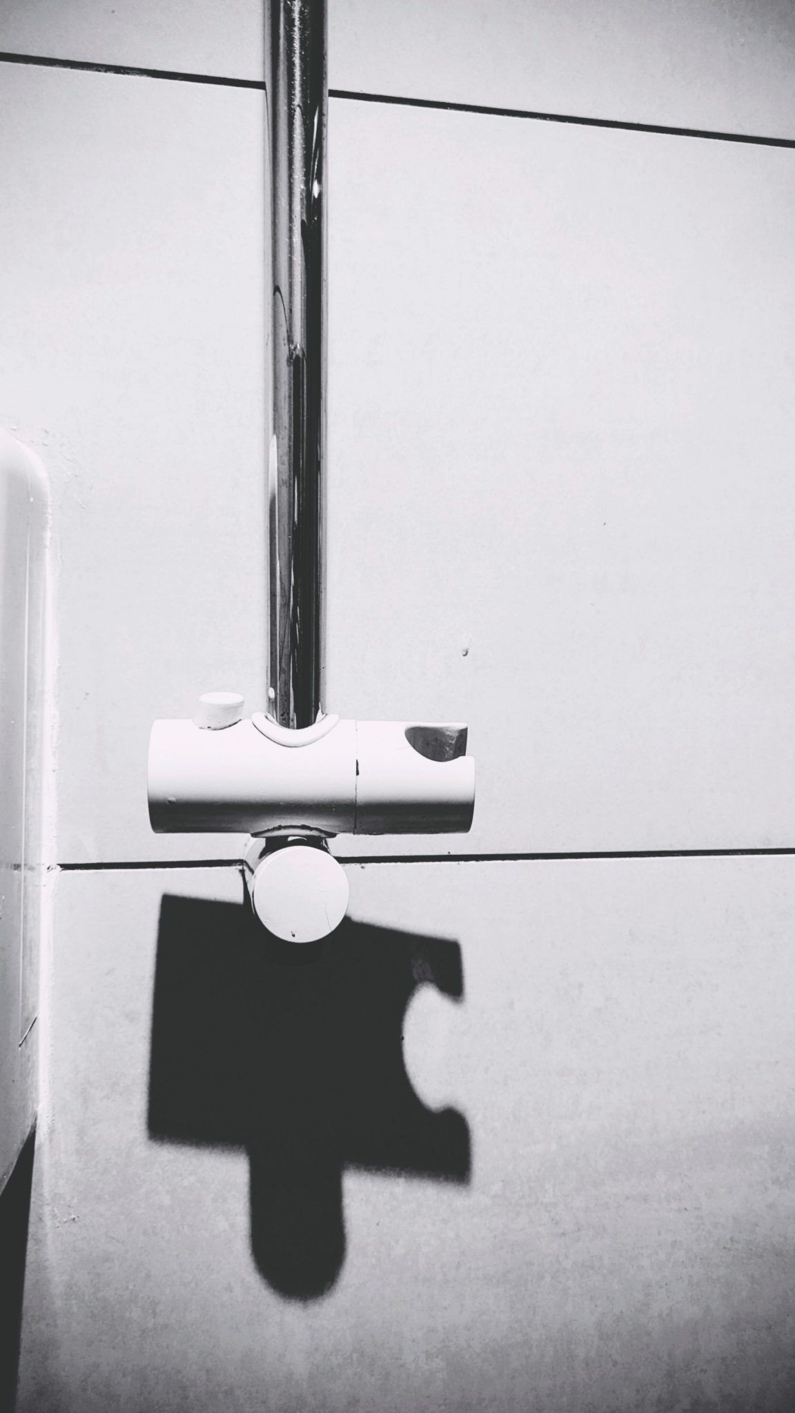 a picture of the shadow the bit that holds a shower head makes onto the tile, which happens to look like a piece of a puzzle. greyish colours and whitish tile colour