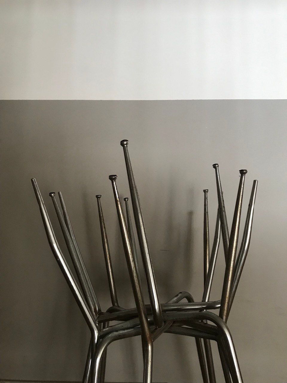 A photo shows three metal chairs' frames put upside down on another chair frame. Background: a gray and white wall.