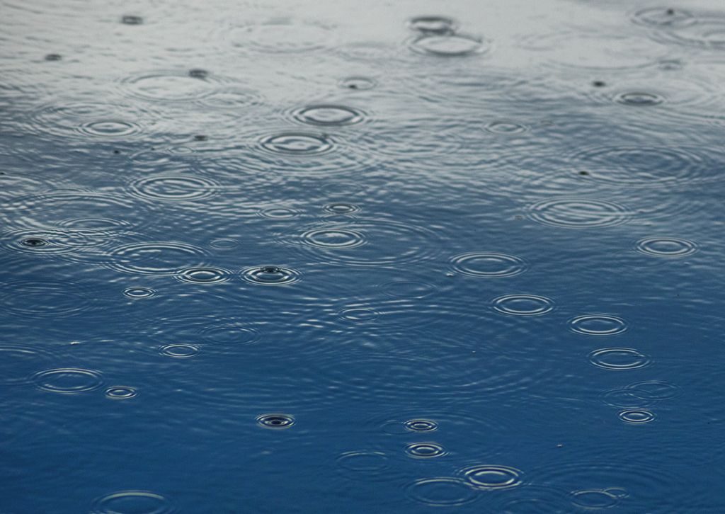 photograph of raindrops landing in a blue and grey puddle
