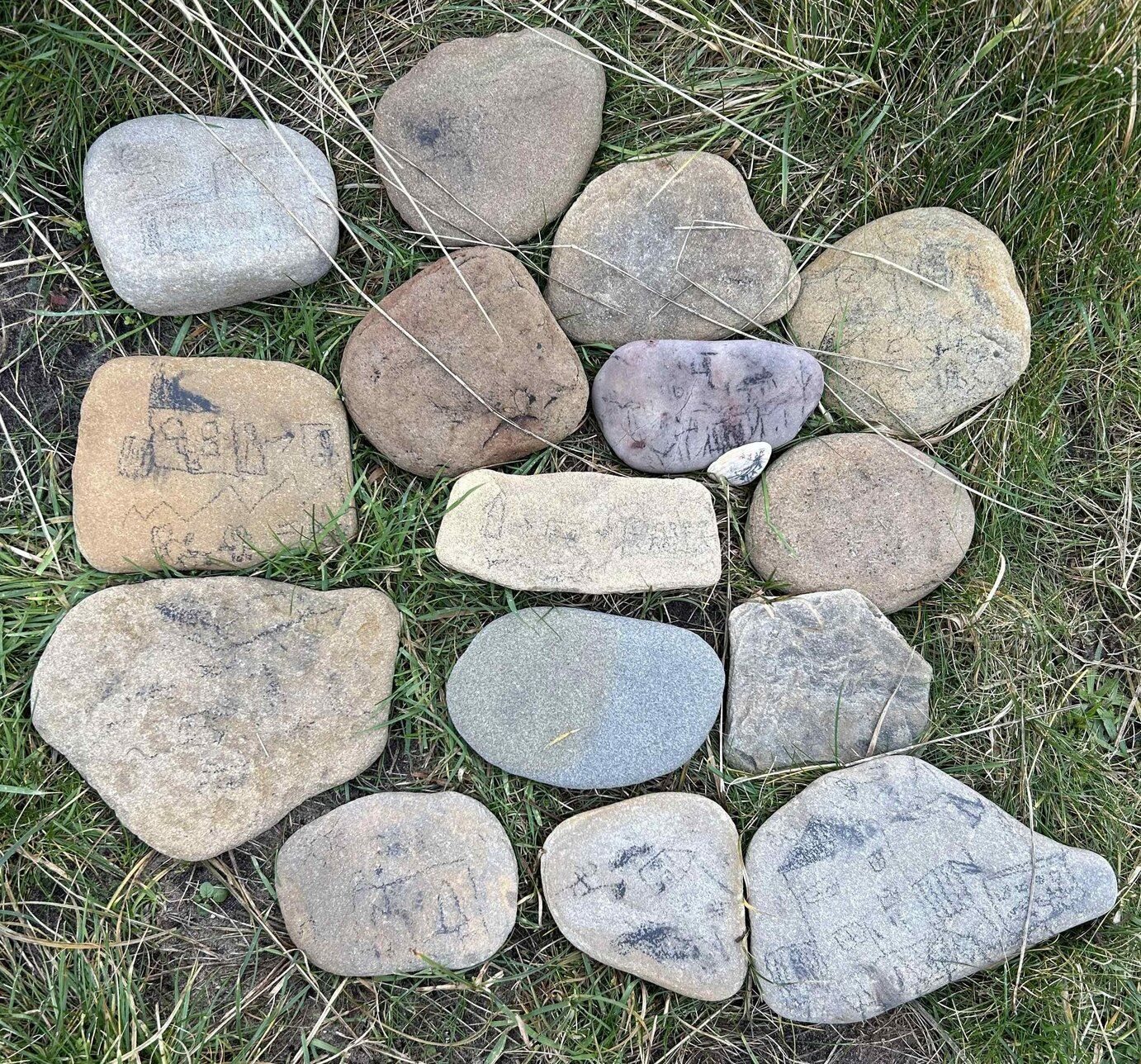 Small flat stones with childrens drawings of houses on them arranged in a circular shape on grass