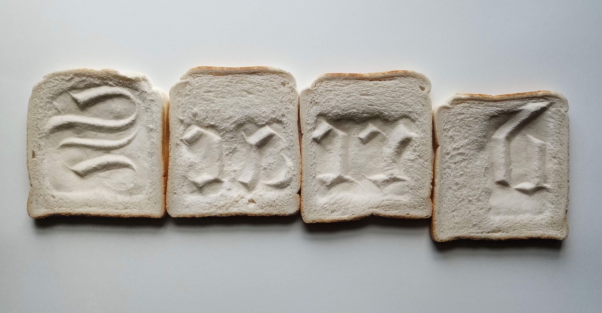 The end of the day is photo of 4 slices of white bread which have impressions of the word 'Sacred' taken from a gravestone.