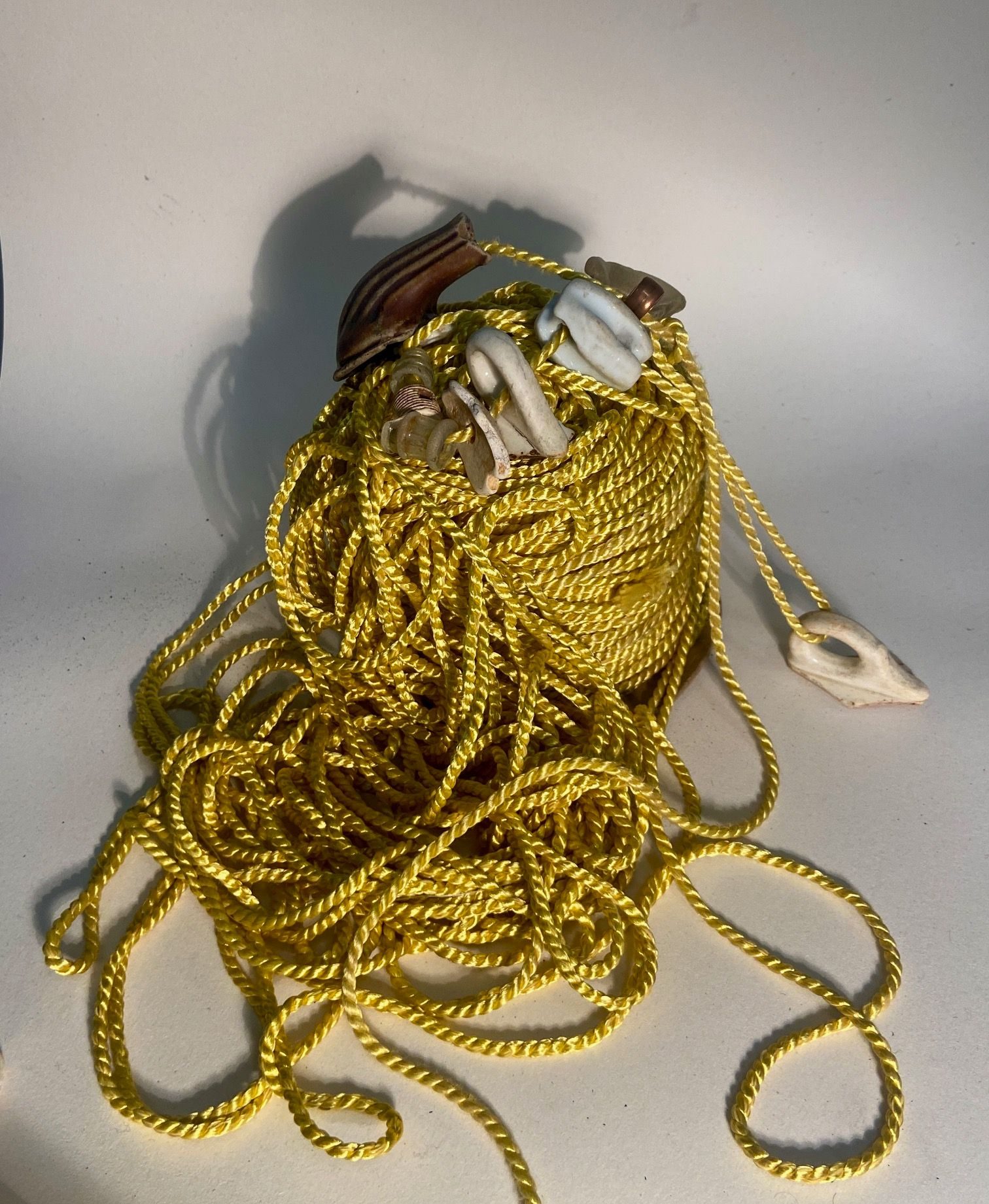 broken cup handles, a teapot spout and other ceramic, glass and copper piping threaded onto an untidy bolt of gold cord